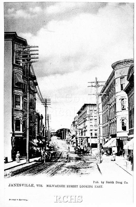 Black and white photograph of Milwaukee Street looking east Pictured: trolley tracks, horses and carriages, power lines Photo description: Janesville, WIS.