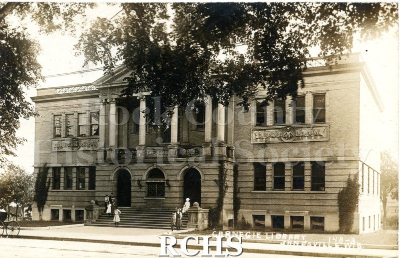 Postcard. Black and white postcard of Carnegie Library in Janesville, Wis. Shows people on steps. Message.
